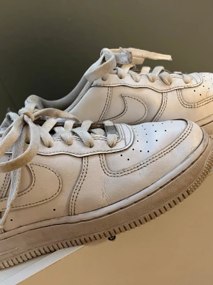 Nike Air Force 1 vita sneakers - Klassiska vita Nike Air Force 1 sneakers i läder med ikonisk swoosh på sidorna och AIR-detalj på hälen. Lågt skaft, perforerad tå och robust gummisula. Ena skor har Sean Banans signatur som tyvärr inte gick bort i tvätten.