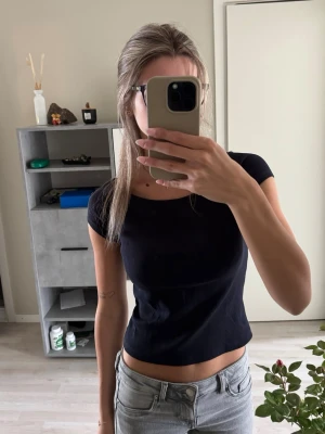 Mörkblå croppad ribbad topp - Snygg mörkblå croppad topp med ribbad struktur och korta ärmar. Toppen har en rund halsringning och sitter figurnära. Perfekt att matcha med jeans eller kjol. Säljer då den inte kom till användning.