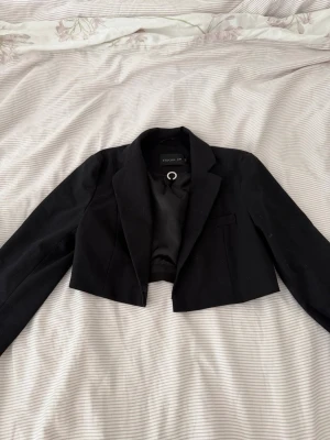 Kort svart kavaj från STOCKH LM - Säljer min Snygga kort svart kavaj från STOCKH LM med klassisk krage och enkel knäppning. Kavajen har en croppad passform och är fodrad med slätt tyg. Perfekt för att lyfta din outfit med en stilren touch. Köpt för 1200kr 
