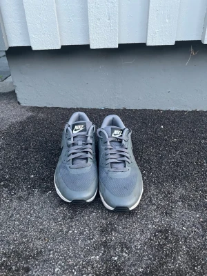 Grå Nike Air Max sneakers - Snygga grå Nike Air Max sneakers med klassisk siluett. Skorna har mesh- och syntetmaterial för bra andningsförmåga och komfort. Tidlös design med Nike-logga på plös och häl. Perfekta för dig som gillar streetwear och sportig stil. Obs sulorna saknas i skorna.