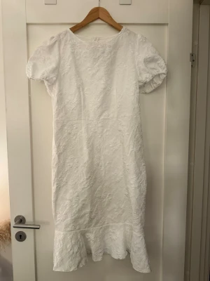 Vit spetsklänning med volang SHEIN - Elegant vit klänning med korta puffärmar och vacker spetsdetalj över hela plagget. Klänningen har en feminin volang längst ner och en rak passform som ger en stilren look. Perfekt för sommarens alla tillfällen. Klänningen är för i för sig lite stor även fastän den har storleken L/40.
