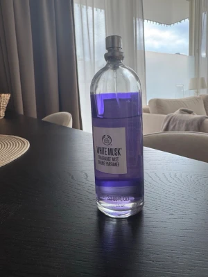 White Musk Fragrance Mist The Body Shop - White Musk Fragrance Mist från The Body Shop i en genomskinlig glasflaska med metallfärgad spraykork. Innehållet är lila och flaskan har en enkel, modern etikett. Perfekt för dig som gillar fräscha och mjuka dofter.