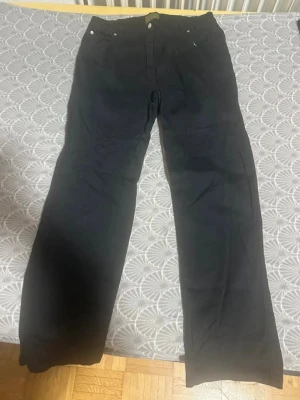 Svarta raka jeans - Säljer ett par svarta jeans med rak passform och klassisk femficksdesign. Jeansen har knappgylf och silverfärgade nitar. Perfekta för dig som gillar en enkel och stilren look. Materialet ser ut att vara bomullsdenim.