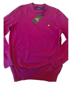 Vinröd stickad tröja Lyle & Scott - Vinröd stickad tröja från Lyle & Scott med rund halsringning och klassisk gul logga på bröstet. Tröjan har långa ärmar och ribbade muddar vid ärmslut och nederkant. Perfekt för dig som gillar stilrena och bekväma plagg.helt ny med prislapp. Storlek Xs