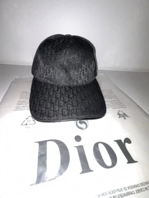 Svart keps med monogram  - Snygg svart keps med all-over monogrammönster och justerbart band bak i läder med logga. Klassisk böjd skärm och stilren design som passar till streetwear och trendiga outfits.