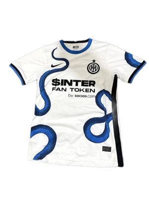 Inter Milan 2021/22 - Snygg vit bortatröja från Inter Milan säsongen 2021/22, designad av Nike. Tröjan har blå ormmönster, svarta detaljer och klubbmärke på bröstet. Tillverkad i lätt och ventilerande material, perfekt för fotboll eller träning.