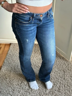 Blå bootcut jeans från LTB - Säljer ett par blå bootcut jeans från LTB med lätt slitna detaljer och klassisk femficksmodell. Jeansen har normal midja och stängs med knapp och dragkedja. Perfekta för dig som gillar en avslappnad men ändå trendig look.