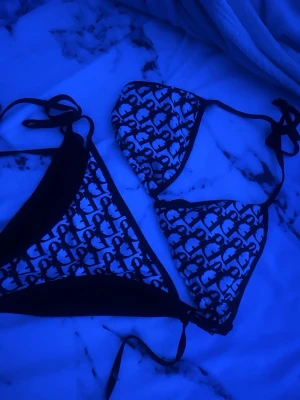 Svartvit bikini med mönster och knyt - Säljer en snygg trekantsbikini i svart och vitt med trendigt mönster. Både överdel och underdel har knytband i sidorna och runt nacken. Perfekt för stranden eller poolen, ger en cool och ungdomlig vibe.