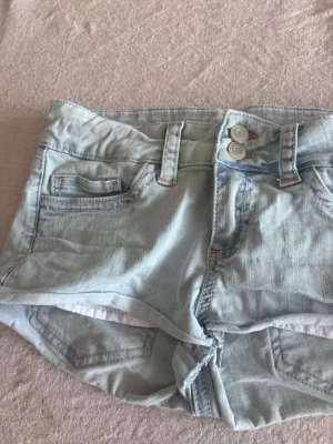 Ljusblå jeansshorts från Nelly - Snygga ljusblå jeansshorts från Nelly med dubbla knappar framtill och klassiska fickor. Shortsen har bälteshällor och en avslappnad passform, perfekta för varma dagar. Tillverkade i mjuk bomull för skön känsla.