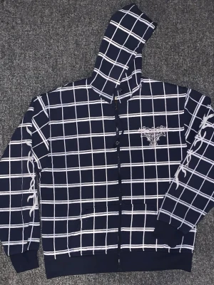 Marinblå rutig hoodie från Kent - Sitter som L-XL. Snygg marinblå hoodie från Kent Collection med vitt rutmönster och dragkedja framtill. Har en broderad detalj på bröstet och två fickor. Tillverkad i mjukt material och har huva med tryckt logga på insidan. Perfekt för en chill och avslappnad stil.