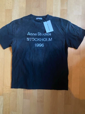 Svart Acne Studios t-shirt  - Snygg svart t-shirt från Acne Studios med tryck 'Acne Studios STOCKHOLM 1996' på bröstet. Klassisk passform och rund hals. Perfekt för dig som gillar stilrena och trendiga plagg med streetkänsla.