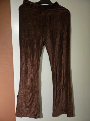 Brunt velour loungewear-set - Mysigt loungewear-set i mjuk brun velour. Setet består av ett par utsvängda byxor med resår i midjan och en matchande hoodie med dragkedja och huva. Perfekt för chill dagar hemma eller när du vill vara extra bekväm.