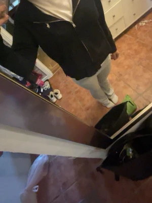 Svart hoodie med dragkedja - Säljer en svart hoodie med dragkedja och huva. Hoodien har två fickor framtill och en liten vit logga på bröstet. Perfekt för chill dagar eller när du vill ha en enkel och stilren look. Materialet känns mjukt och bekvämt.