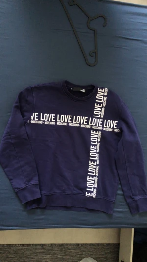 Moschino - Mörkblå sweatshirt från Moschino med vita texter 'LOVE’ och ’MOSCHINO' över bröstet och ner längs sidan. 