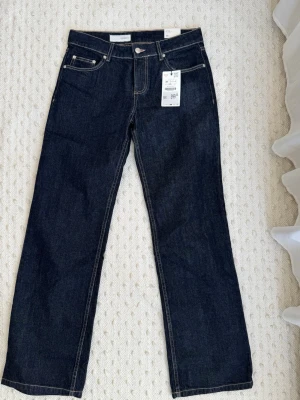 Mörkblå baggy jeans low rise - Säljer ett par mörkblå jeans med wide passform och låg midja. Klassisk femficksmodell med kontrastsömmar och knappgylf. Perfekta till vardagslooken och lätta att matcha med olika stilar.