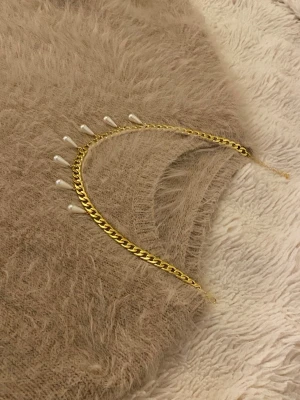 Guldhalsband med droppformade pärlor - Snyggt halsband i guldfärgad rostfritt med sju droppformade vita pärlor som hänger längs kedjan. Kedjan har en chunky design och ger ett trendigt intryck. Perfekt för dig som vill ha något som sticker ut och känns modernt.