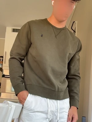 Olivgrön sweatshirt från Polo Ralph Lauren - Snygg olivgrön sweatshirt från Polo Ralph Lauren med rund halsringning och diskret broderad logga på bröstet. Tröjan har ribbade muddar vid ärmslut och nederkant, perfekt för en avslappnad och stilren look.