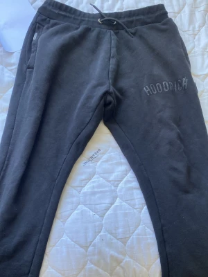 Svarta mjukisbyxor från Hoodrich - Säljer ett par svarta mjukisbyxor från Hoodrich med broderad logga på vänster ben. Byxorna har dragsko i midjan och sidofickor. Perfekta för chill dagar och streetwear-stil. Tillverkade i mjukt material för maximal komfort.