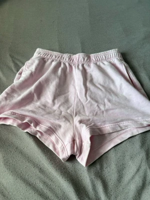 Ljusrosa mjuka shorts med resår - Säljer ett par ljusrosa shorts med elastisk midja och avslappnad passform. Shortsen har fickor på sidorna. Perfekta för varma dagar eller att chilla i hemma.