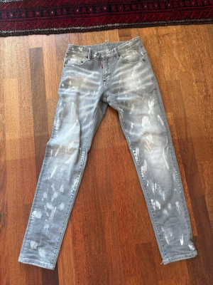 Grå DSQUARED2 jeans - Snygga grå DSQUARED2-jeans med en distinkt design med vita färgstänk och avsiktligt slitage för en modern, sliten estetik. Pris kan diskuteras.  ⭐️ Skick: 8/10  🎲 Storlek: 29 🎨 Färg: Grå med vita stänk 📦 Snabb och noggrann leverans