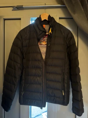 Svart dunjacka med gul detalj - Säljer en mörkblå dunjacka från Parajumpers i kategorin ”Super Light Weight”. Perfekt för höst-/vårdagar  och riktigt snygg till streetwear-stilen. Jackan har två små hål på höger ärm som har överlappats med tygmaterial i liknande nyans (se bild) men är annars i väldigt gott skick! Med hjälp av QR-koden på insidan av jackan kan du också säkerställa att produkten är äkta från Parajumpers.