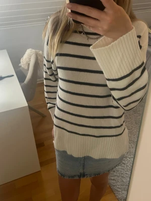 Vit stickad tröja med svarta ränder - Snygg vit stickad tröja med svarta horisontella ränder och breda ribbade muddar vid ärmslut och nederkant. Tröjan har en avslappnad passform och rund halsringning. Perfekt för en stilren och trendig look.