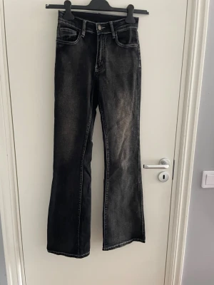 Svarta bootcut jeans med broderi - Säljer ett par svarta bootcut jeans med snygg tvätt och vita broderade detaljer på bakfickorna. Jeansen har klassisk femficksmodell, knappgylf och kontrastsömmar. Perfekta för dig som gillar en avslappnad men trendig look.