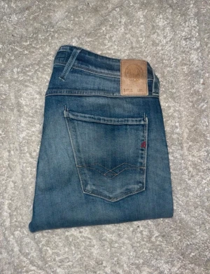 Replay Anbass jeans  - Snygga blå slim fit jeans från Replay med klassisk femficksmodell och diskreta slitningar. Jeansen har en läderpatch med Replay-logga bak i midjan och kontrastsömmar på bakfickan. Tillverkade i mjuk denim för en bekväm känsla.Längd storleken saknas men bedömd till L34 men skulle även kunna vara långa L32. JAG SKICKAR EJ FLER BILDER PÅ JEANSEN! för storleksguide hänvisar jag till måtten och för bättre inblick i passformen rekommenderar jag att googla på modellnamnet. :) 1,101