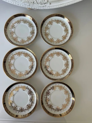 Sex vita assietter med gulddetaljer - Ett set om 6 fat från Hartporzellan, tillverkade i Tyskland. Faten är vita med detaljer i guld och svart. Guldmönstret är snirkligt och elegant, medan den svarta kanten har ett geometriskt mönster. 