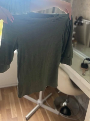 Grön ribbad topp med trekvartsärm - Snygg grön ribbad topp med trekvartsärm och rund hals. Toppen har en enkel och stilren design som passar perfekt till jeans eller kjol. Materialet känns mjukt och följsamt mot kroppen.