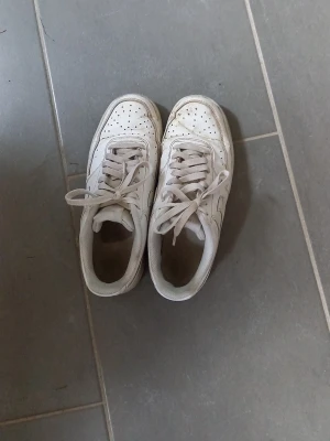 Vita klassiska sneakers - Säljer ett par vita sneakers med lågt skaft och snörning. Skorna har perforerade detaljer på tån och en enkel, stilren design. Tillverkade i syntetmaterial och passar perfekt till streetwear eller casual outfits.