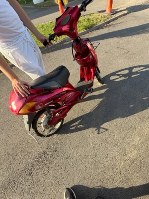 Röd elcykel/moped med svart sadel - Säljer en röd elcykel eller elmoped med svart sadel och silverfärgade detaljer. Modellen har en klassisk design med fotstöd, pakethållare och breda hjul. Perfekt för att ta sig fram snabbt i stan.