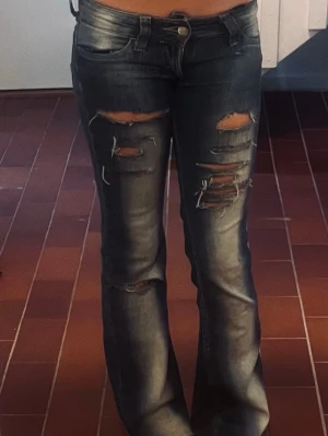 Blå slitna bootcut jeans - Kvarg jeans stolek 24/30 sitter som 25/30Säljer ett par blå bootcut jeans med flera slitningar och hål på framsidan. Jeansen har klassisk femficksmodell, låg midja och är tillverkade i denim. Perfekta för en avslappnad och trendig look.