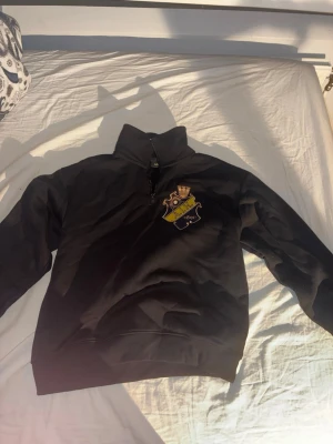Svart AIK hoodie med halv dragkedja - Svart hoodie från AIK med klubbens emblem broderat på bröstet. Tröjan är inte använd en ända gång eftersom jag beställde den men så var den för stor och det var minsta storleken. Tröjan har halv dragkedja framtill och hög krage. Tillverkad i mjukt material som känns skönt mot huden. Perfekt för dig som vill visa ditt AIK-stöd med stil.