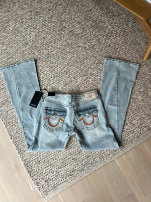 True Religion Joey low rise flare jeans - Säljer ett parhelt nya jeans med prislapp från true religion som enligt true religion flare men jag upplever mer åt bootcut hållet från True Religion med kontursömnar och broderade fickor bak. Jeansen har fem fickor, knappgylf och detaljer i silver och koppar. Strl W26. Nytt par kostar 1299kr