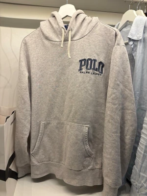 Grå hoodie från Polo Ralph Lauren - Snygg ljusgrå hoodie från Polo Ralph Lauren med broderad logga i blått på bröstet. Perfekt för en avslappnad och stilren look.