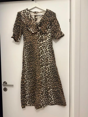 Leopardmönstrad klänning från Ganni - Aldrig använd men tagit bort lappen. Nypris 3400:-. Säljer en snygg leopardmönstrad klänning från Ganni med volangkrage och korta ärmar. Klänningen har en figurnära passform upptill och är lätt utsvängd nertill. Materialet känns mjukt och följsamt, perfekt för dig som vill sticka ut med ett djurmönster.