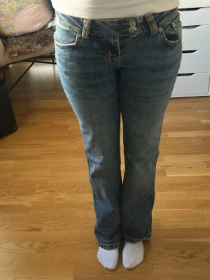 Blå bootcut jeans från 157 - Ett par klassiska blå bootcut jeans från 157 med fem fickor och snygga kontrastsömmar. Jeansen har normalhög midja och är tillverkade i denim med lätt tvättad look. Perfekta för en avslappnad och trendig stil. Lite slitna vid fötterna