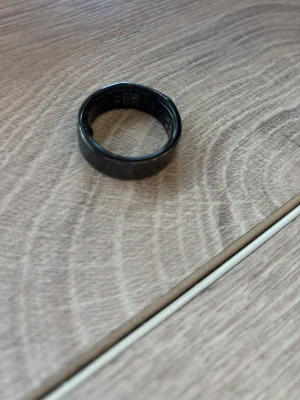 Svart smart ring från Oura - En svart smart ring från Oura i slimmad och modern design. Ringen är tillverkad i ett tåligt material och används för att mäta hälsa och aktivitet, som sömn och puls. Perfekt för dig som vill ha koll på din hälsa utan att bära armband. Obs bara ringen tillkommer