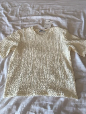Vit t-shirt från AIIZ, regular fit - Vit t-shirt från AIIZ i regular fit, storlek M. T-shirten har en klassisk rund halsringning och är tillverkad i ett strukturerat tyg som ger en unik känsla. Perfekt för dig som gillar stilrena och bekväma plagg.