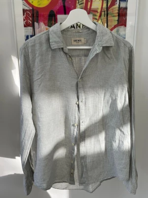 Ljusgrå randig linneskjorta East West - Snygg ljusblå skjorta från East West i linnemix. Skjortan har diskreta ränder, klassisk krage och knäppning framtill. Perfekt för en avslappnad men stilren look.