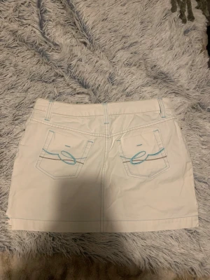 Vit kortkjol med blå detaljer - Säljer en vit kortkjol med ljusblå sömmar och broderade detaljer på bakfickorna. Jätte fin nu till sommaren🌸 kjolen är instorlek M, kan tyvärr inte skicka bild på då den är för liten för mig. Aldrig använt den, köpte den här ifrån men den är i fint skick!🫶🏽
