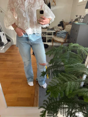 Ljusblå ripped straight leg jeans - Säljer ett par ljusblå jeans med raka ben och stora slitningar vid knäet. Jeansen har hög midja och klassisk femficksmodell. Perfekta för en avslappnad och trendig look.