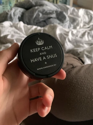 Svart snusdosa med text - Säljer en svart snusdosa i plast från Swedsnus med texten 'KEEP CALM AND HAVE A SNUS' på locket. Dosan har rund form och är perfekt för att förvara snus eller småsaker. Enkel att öppna och stänga, smidig att ha med sig i fickan.