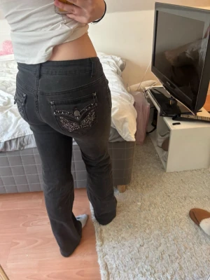 Svarta bootcut-jeans med detaljer - Säljer ett par svarta bootcut-jeans med snygga fickdetaljer bak och nitar framtill. Jeansen har hög midja och är i stretchigt denimtyg. Perfekta för dig som gillar en cool och trendig look.