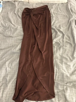 Brun omlott långkjol med slits  - Snygg brun långkjol i omlottmodell med knyt framtill och slits. Kjolen har en elegant drapering och är gjord i ett mjukt, glansigt material. Köpt på SHEIN i xs, aldrig använd 