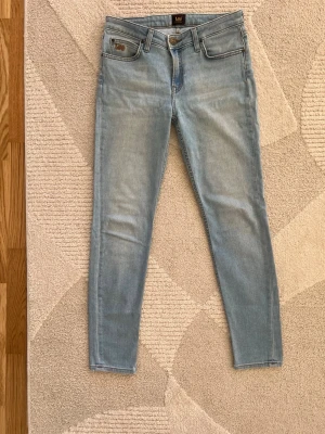 Ljusblå skinnymodell jeans från Lee - Snygga ljusblå skinny jeans från Lee med klassisk femficksdesign och dragkedjegylf. Jeansen har Lee-logga på fickan och är tillverkade i stretchigt denimtyg för en bekväm passform. Perfekta till en avslappnad stil.