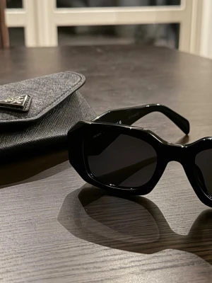 Svarta solglasögon från Prada - Snygga svarta solglasögon från Prada med breda, rektangulära bågar i blank plast. Klassisk och trendig design som ger en cool vibe. Kommer med originalfodral med Prada-logga. Använd några månader av min sambo. Fint skick 