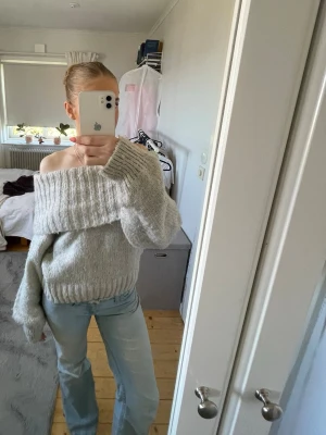 Ljusgrå off shoulder stickad tröja - Säljer en ljusgrå stickad tröja med bred off shoulder-krage och långa, lösa ärmar. Tröjan har ribbstickade muddar vid ärmslut och nederkant. Perfekt för dig som gillar en avslappnad och trendig stil😊