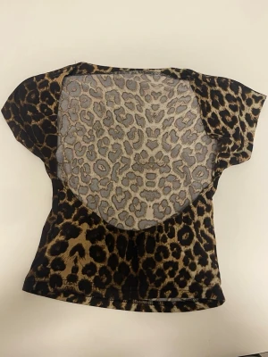 Leopardmönstrad topp med kort ärm - Cool topp med leopardmönster i bruna och svarta toner. Modellen har korta ärmar och en figurnära passform. Perfekt för dig som vill sticka ut med ett djurmönstrat plagg. Materialet känns stretchigt och mjukt.